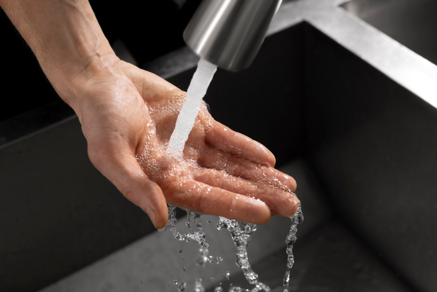 clean drinking water flowing from a kitchen faucet into a person’s hands