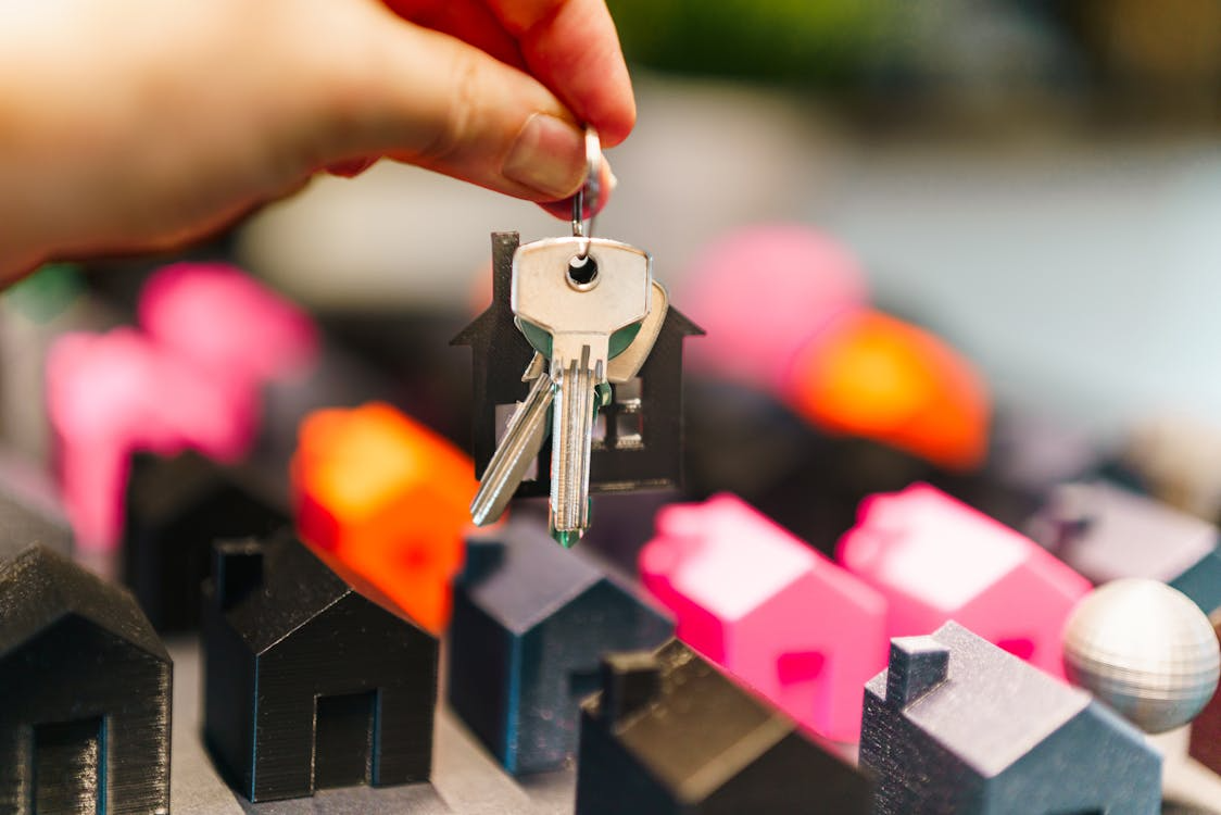 Hand holding keys and miniature home models, representing renting vs buying a home decision